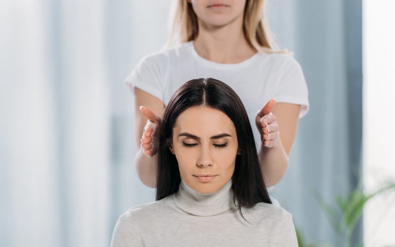cropped shot of peaceful young woman with closed eyes sitting and receiving reiki healing therapy